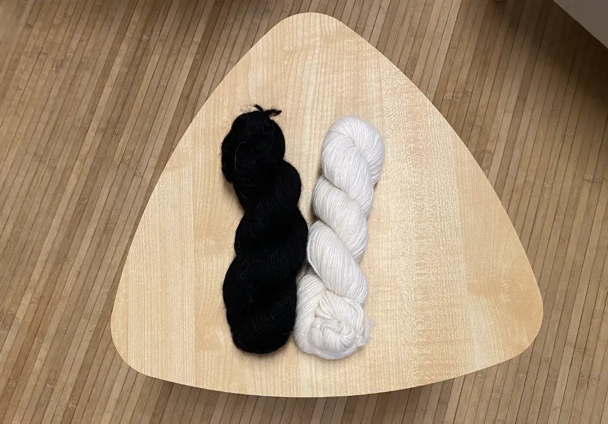 ein schwarzer und ein weißer Strang des Alpaka-Garns "Puna" liegen nebeneinander auf einem kleinen Holztisch