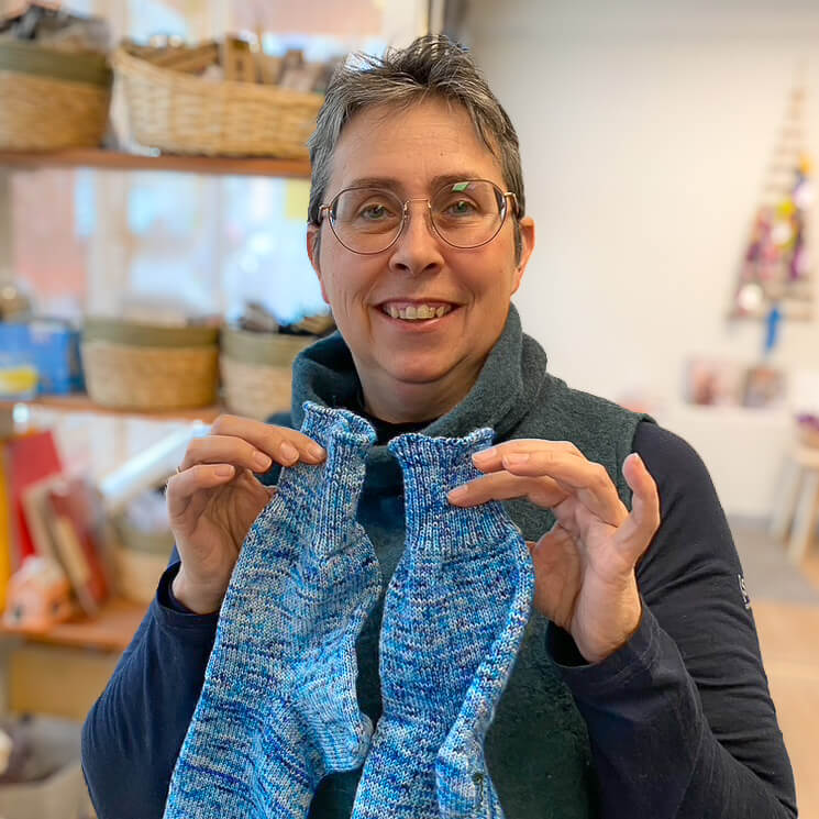Portrait von Daniela Körner im Wollkorb, dem Wolleladen in Pfullingen Portrait von Daniela Körner im Wollkorb in Pfullingen mit zwei blauen, selbstgestrickten Socken in der Hand