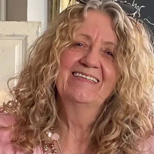 Portrait von Sylvia Jogsch, die mit ihren langen blonden, lockigen Haaren offen in die Kamera lacht.